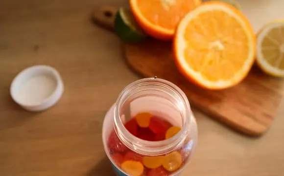 A jar of vitamin gummies beside fresh oranges — dietary supplements